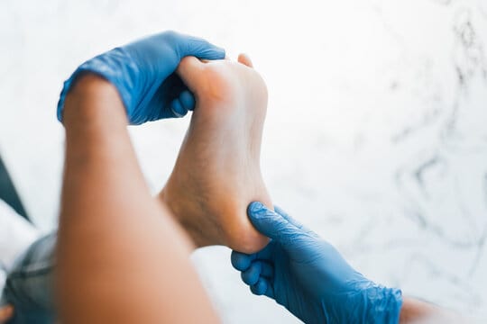 Close up of a podiatrist hands with medical gloves exploring the foot of a patient in the podiatry c