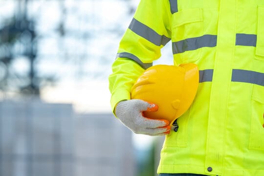 Construction engineer holding yellow safety helmet at work on construction site.