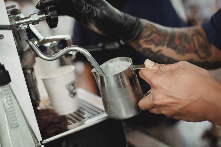 Crop faceless barista frothing milk with steam wand